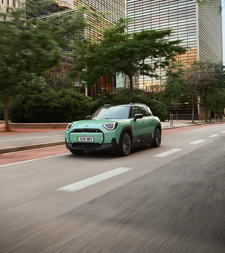 All‑electric MINI Aceman in Rebel Green driving through a city street