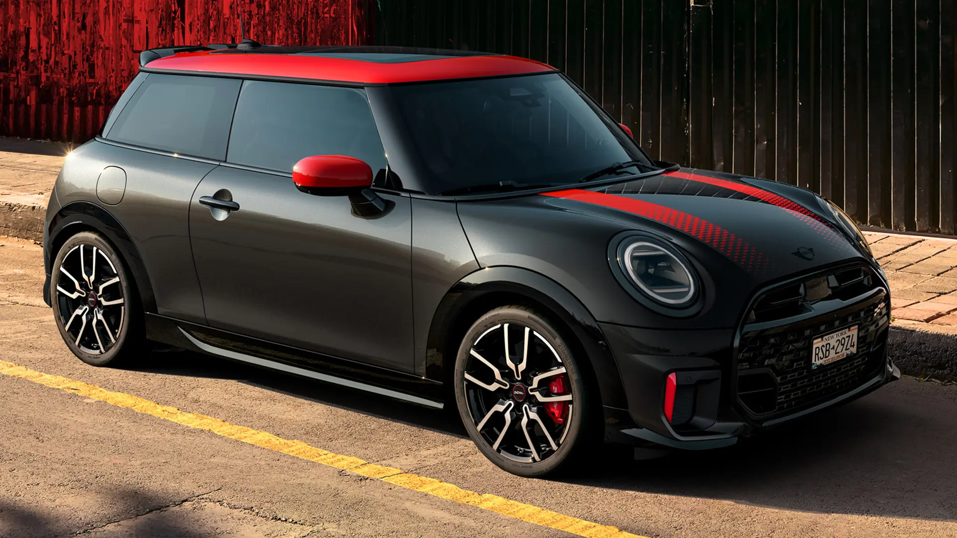 MINI John Cooper Works 3ja dyra í Midnight Black með Chili Red þaki og speglahlífum og rauðum sportröndum, hliðarsýn, lagt í götu.